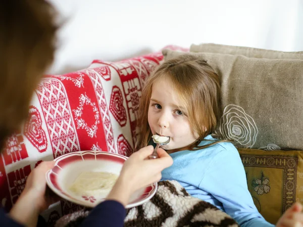 Mother feeding taken ill daughter by semolina — Stock Photo, Image