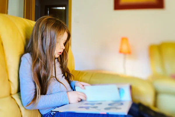 Cute little girl with long hair reading children book in livivng — Stock Photo, Image