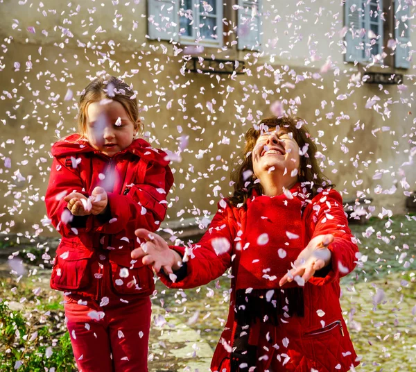 Madre con hija pequeña jugando con pétalos que caen primavera d — Foto de Stock