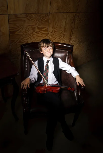 Piegowaty czerwono włosy chłopak z skrzypce, siedząc w fotelu — Zdjęcie stockowe