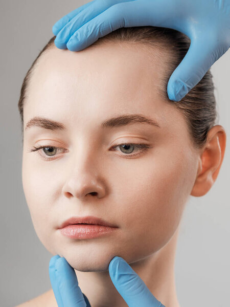 Косметические процедуры для молодого красивого женского лица, рука врача в перчатках касаются лица женщины, изолированной на белом. Уход за кожей, косметологические процедуры, воск для тела, норковая ресница, уход за бровями, постоянный