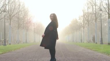 Güzel genç bir kadın sabah sisli parkta model yürüyüşü yapar. Kış başlarında, sonbahar kıyafetleri giyer.