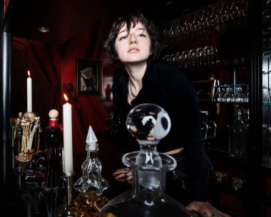 Gotik tarzda giyinmiş genç bir kız, kırmızı ve siyah renkli lüks bir alkolik barda poz veriyor. Karşıtlık.