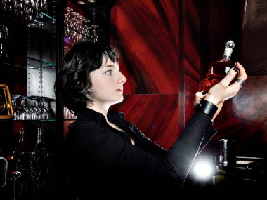 Gotik tarzda giyinmiş genç bir kız, kırmızı ve siyah renkli lüks bir alkolik barda poz veriyor. Karşıtlık.