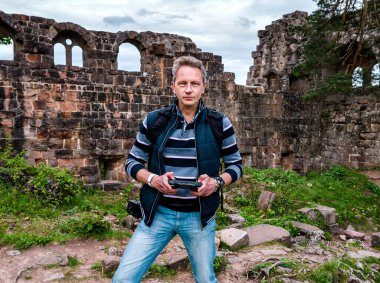 İnsansız hava aracını kontrol eden bir adam, ortaçağdan kalma bir şatonun harabelerinde, dağların ortasında kendini fotoğraflıyor. Fransa