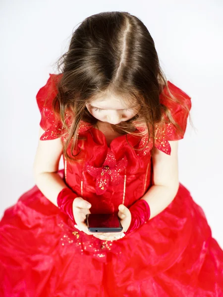 Schattig klein meisje gekleed in bal toga spelen met smartphone — Stockfoto