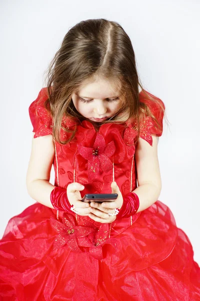 Søt liten jente kledd i ballkjole som leker med smarttelefon – stockfoto