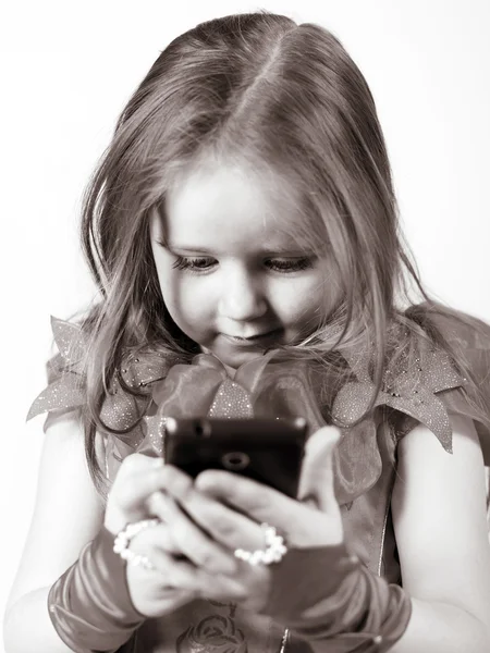 Schattig klein meisje gekleed in bal toga spelen met smartphone — Stockfoto