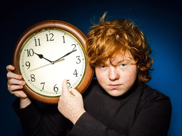 Expressive red-haired teenage boy showing time on big clock — Stock Photo, Image