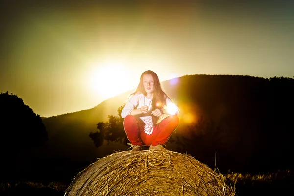 Adolescente posant le soir sur une botte de foin, couleurs du coucher de soleil — Photo