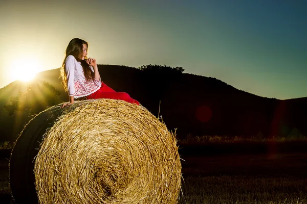 Adolescente posant le soir sur une botte de foin, couleurs du coucher de soleil — Photo