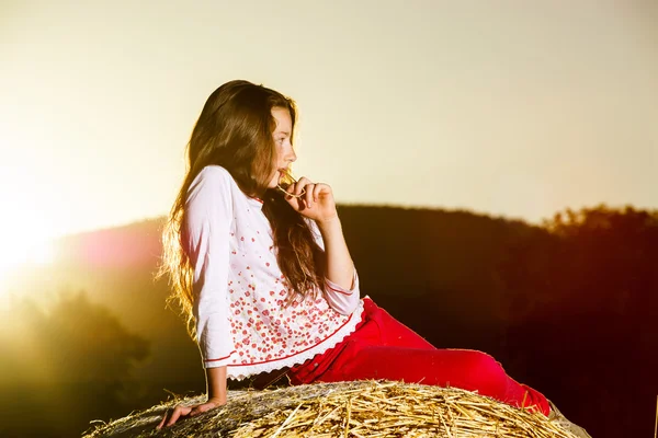 Adolescente posant le soir sur une botte de foin, couleurs du coucher de soleil — Photo