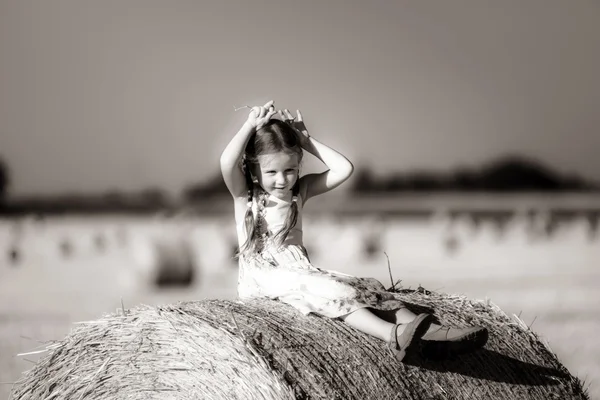 Petite fille mignonne drôle posant sur la meule de foin dans le champ d'été — Photo