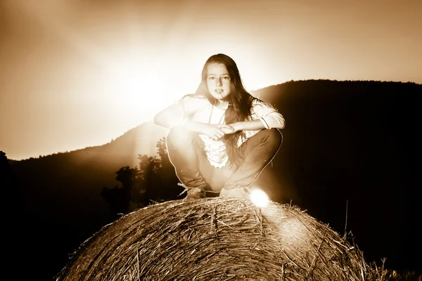 Adolescente posando en la noche en el pajar, los colores de la puesta del sol — Foto de Stock