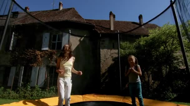 Twee zussen springen op de trampoline in achtertuin — Stockvideo