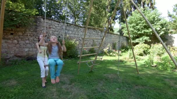 Oudere zus swingende kleinere op wip in de achtertuin — Stockvideo
