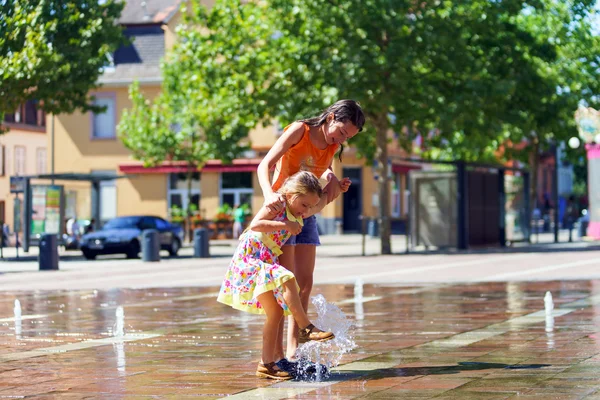 Dos hermanas jugando con salpicaduras de fuente — Foto de Stock