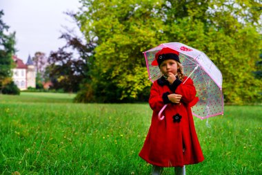 Sevimli küçük kız kırmızı ceket ve yeşil çim alan şapka giymiş