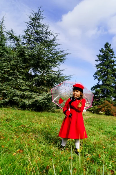 赤いコートと帽子に緑の芝生のフィールを着たかわいい女の子 — ストック写真