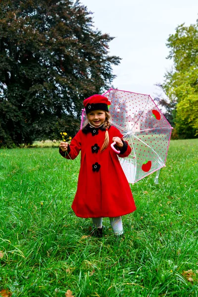 Menina bonito vestido com casaco vermelho e chapéu na grama verde fiel — Fotografia de Stock