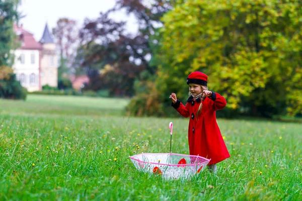 Cute little girl dressed in red coat and hat on green grass fiel — Stock Photo, Image