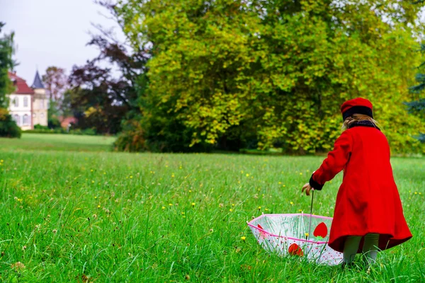 Милая маленькая девочка, одетая в красное пальто и шляпу на зеленом филе травы — стоковое фото
