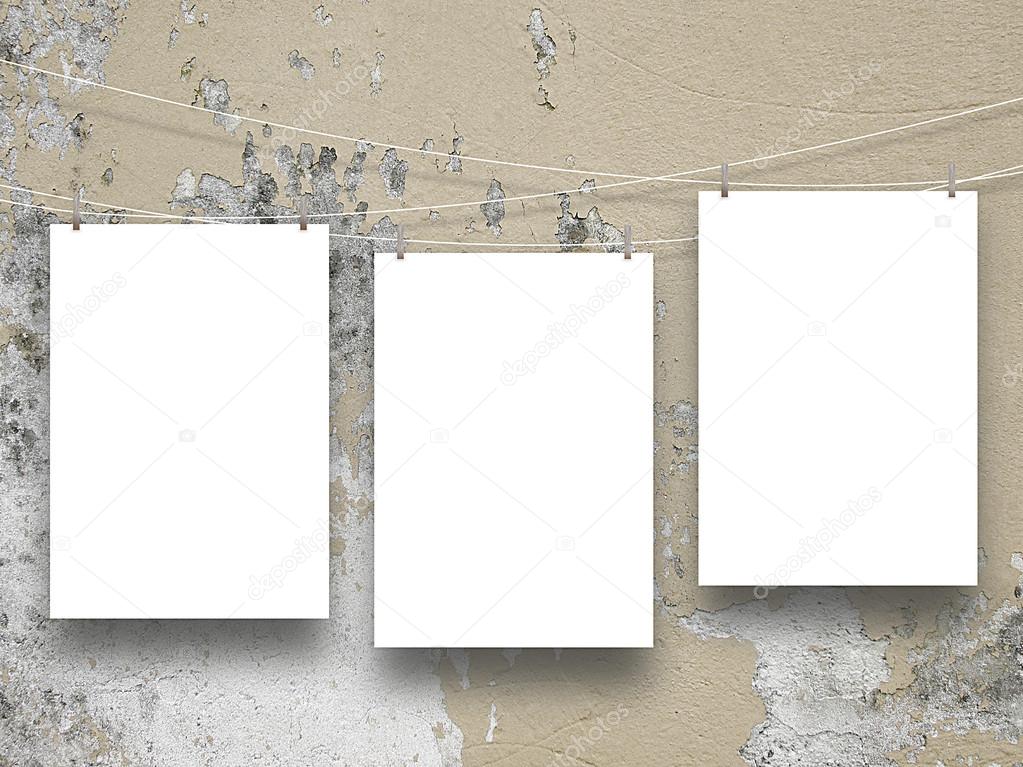 Three empty frames hanged by clothes pins on scratched light brown concrete wall