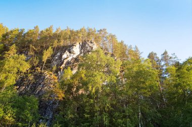 Yeşil ormanları ve mavi gökyüzünün altındaki yüksek kayalık dağları olan güzel bir manzara.