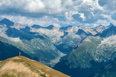 Siyah sırt çantalı bir gezgin büyük dağların tepesinde duruyor. Uzağa bakıyor. Bulutlu resim gibi bir manzara. Montaj hedefiniz için duvar kağıdı, top, iş, konsept düşünme.
