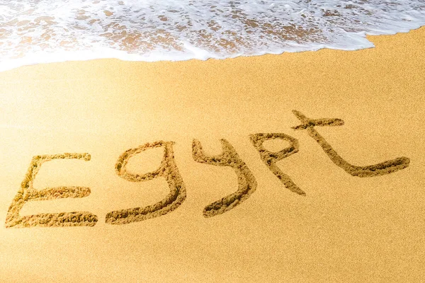 Egypt title on the sand beach of the Red sea. Brilliant sun ray falls on the letters. Hot season. Wave.