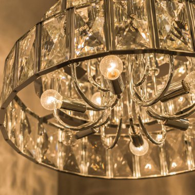 Kristal tavan abajurundan parlayan lüks avizenin yakın çekimi. Modern bir iç mekanda klasik tarz. İçeri gir. Sıcak sarı ışık. Ayrıntılar.