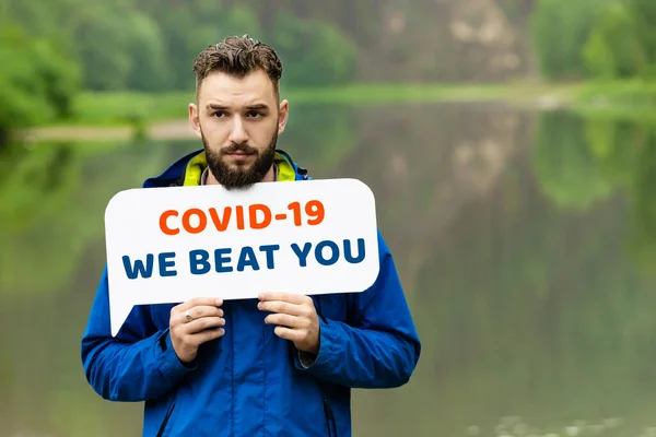 Mavi ceketli genç bir adam yazın kırsalda duruyor ve virüsün mesajını taşıyor. Seni yendik. İlaç ve sağlık hizmetleri. Salgın Konsepti Coronavirüs 2020.