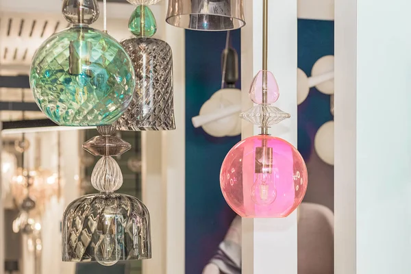 A group of switched-off multicolored lamps with a gray, turquoise, pink glass ceiling is suspended in the white interior. Concept of show room decoration. Inside. Close up. Warm light.