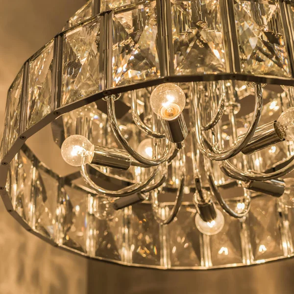 Kristal tavan abajurundan parlayan lüks avizenin yakın çekimi. Modern bir iç mekanda klasik tarz. İçeri gir. Sıcak sarı ışık. Ayrıntılar.