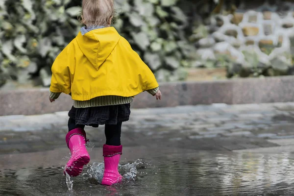 Ein Nettes Kleines Mädchen Gelbem Regenmantel Und Rosafarbenen Gummistiefeln Springt lizenzfreie Stockbilder