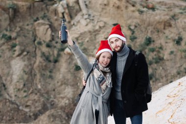 Paltolu ve kırmızı Noel şapkalı genç bir çift dışarıda duruyor ve ellerinde bir şişe şarap tutuyorlar. Mutlu bir yeni yıl konsepti.