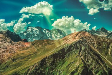 Dev bir dağ yığınının zirvesinde küçük bir adam. Gökyüzündeki güneş ışınları kümülüs bulutlarıyla turistlerin üzerine düşüyor. Zafer.