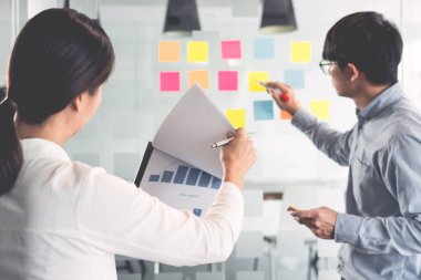 İşletme müdürü kendi takımı için fikir sunuyor ve cam pencere üzerine birçok not yapıştırıyor. İş görüşmeleri, yaratıcı ofis, planlama ve yönetim kavramında başarılı olmak için.