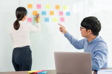 İşletme müdürü kendi takımı için fikir sunuyor ve cam pencere üzerine birçok not yapıştırıyor. İş görüşmeleri, yaratıcı ofis, planlama ve yönetim kavramında başarılı olmak için.