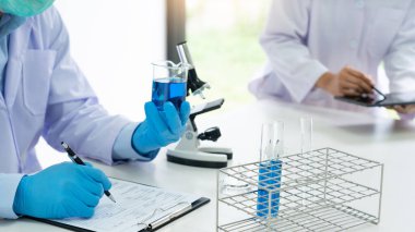 Laboratuvar önlüğü ve güvenlik gözlüğü takmış çekici genç bilim adamları test denemeleri üzerinde çalışıyorlar ya da laboratuvar tüpleriyle araştırma yapıyorlar.