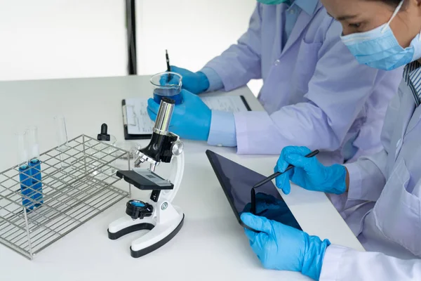 Attractive young scientist team in lab coat and safety goggles working with analysing test trial or investigations with test tubes in laboratory