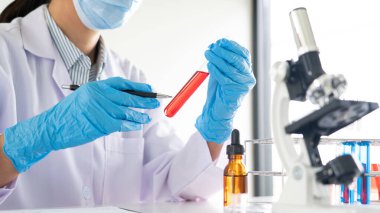 Genç Asyalı bilim adamı mikroskopla inceleyerek adli tıp laboratuarındaki bir deney örneğini analiz ediyor.