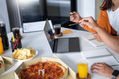 Bir grup iş adamı şirkette birlikte öğle yemeği yemek için proje hakkında konuşuyor ve pizza ve patates cipsi hazırlıyorlar.