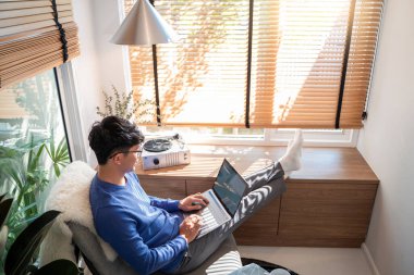 Genç ve çekici Asyalı bir adam evinde rahat rahat dizüstü bilgisayarla çalışıyor. 