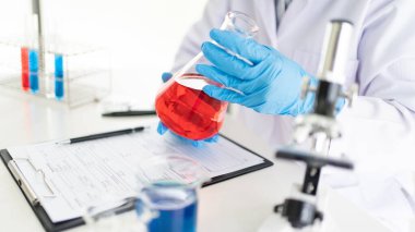 Genç Asyalı bilim adamı mikroskopla inceleyerek adli tıp laboratuarındaki bir deney örneğini analiz ediyor.