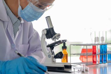 Laboratuvarda beyaz önlükle araştırma yapan bilim adamları eldivenleri analiz ediyor, test tüpleri örneklerine bakıyor, biyoteknoloji kavramına bakıyor..