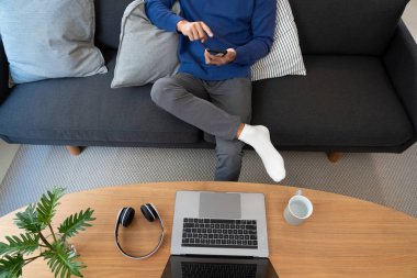 Yakışıklı Asyalı gözlüklü genç adam oturma odasındaki cep telefonuyla interneti tarıyor. 