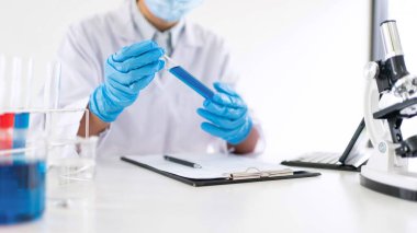 Genç Asyalı bilim adamı mikroskopla inceleyerek adli tıp laboratuarındaki bir deney örneğini analiz ediyor.