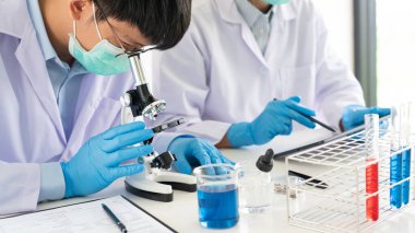 Laboratuvar önlüğü ve güvenlik gözlüğü takmış çekici genç bilim adamları test denemeleri üzerinde çalışıyorlar ya da laboratuvar tüpleriyle araştırma yapıyorlar.