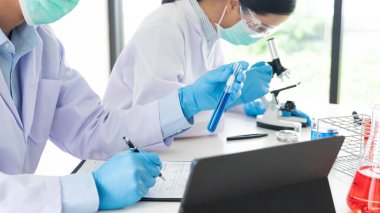 Laboratuvar önlüğü ve güvenlik gözlüğü takmış çekici genç bilim adamları test denemeleri üzerinde çalışıyorlar ya da laboratuvar tüpleriyle araştırma yapıyorlar.